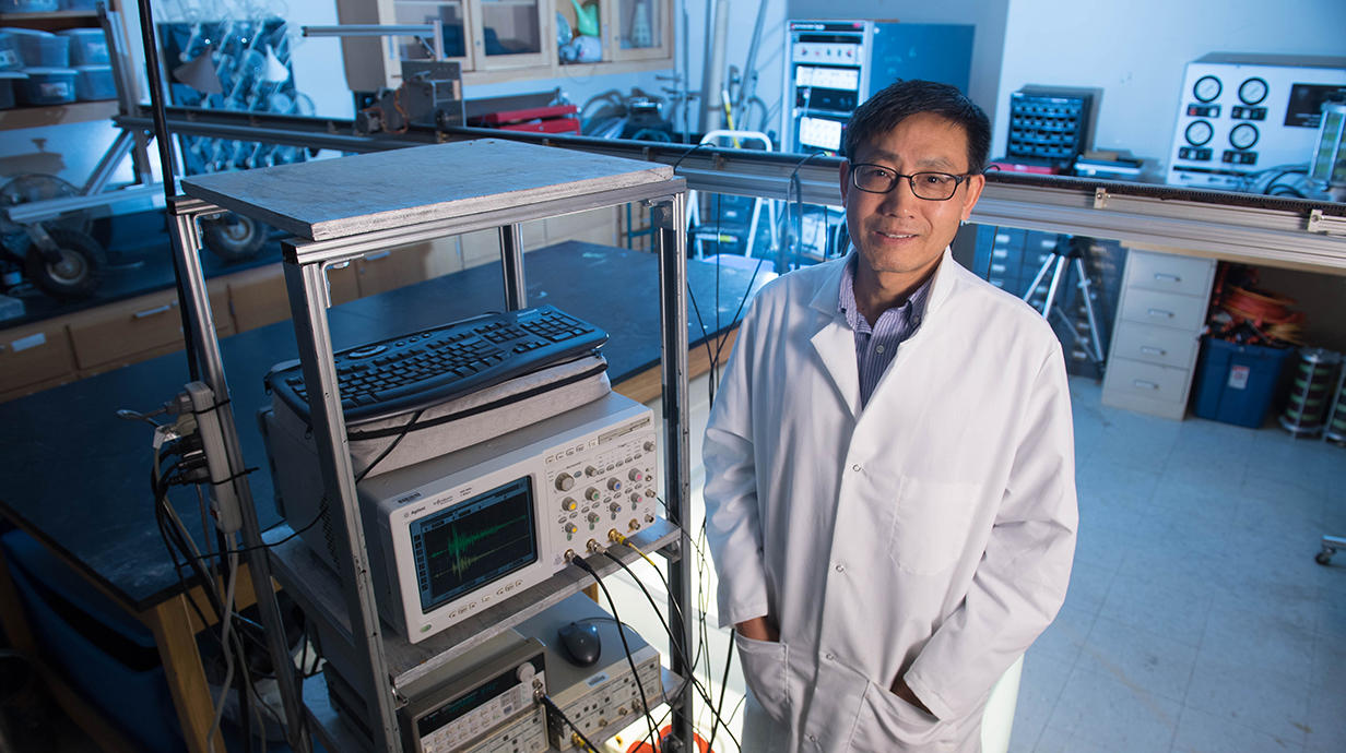 A man wearing a lab coat stands next to a rack of electronic equipment in a laboratory.