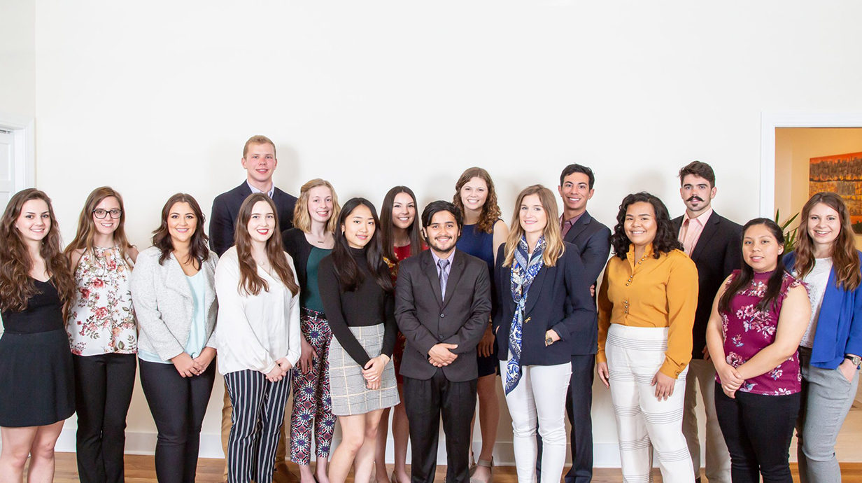 A large group of young people stands in front of a white wall.
