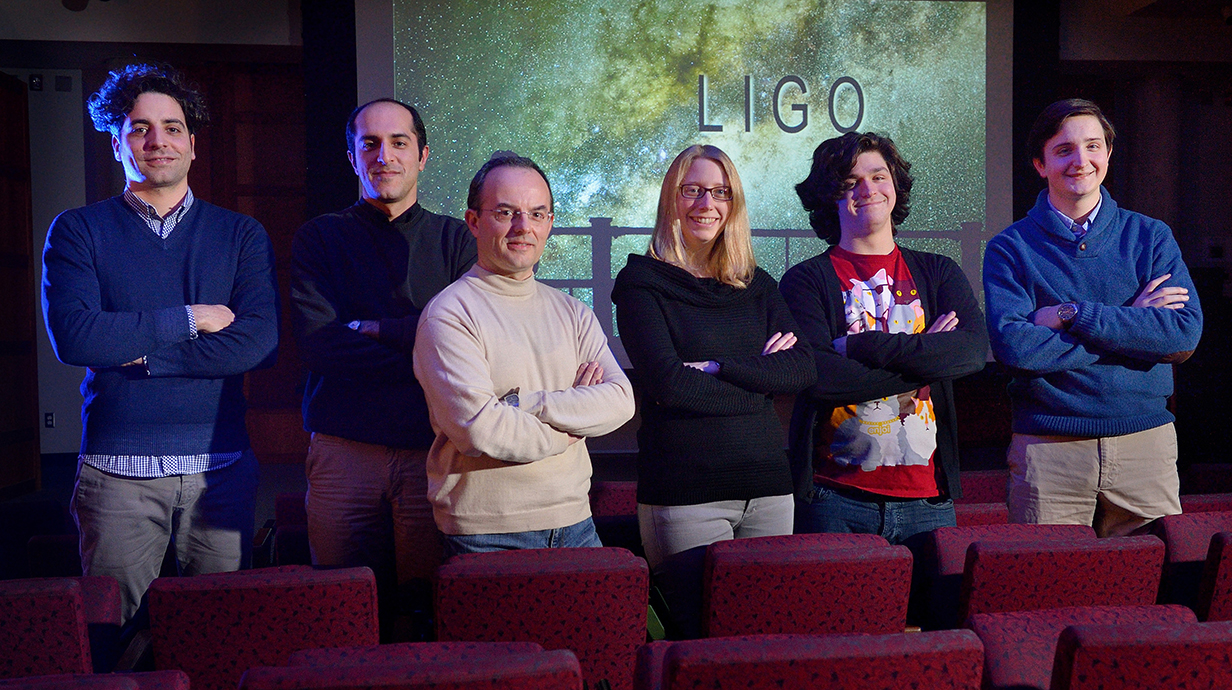 A group of men and women stand in front of a projection screen in a theater.