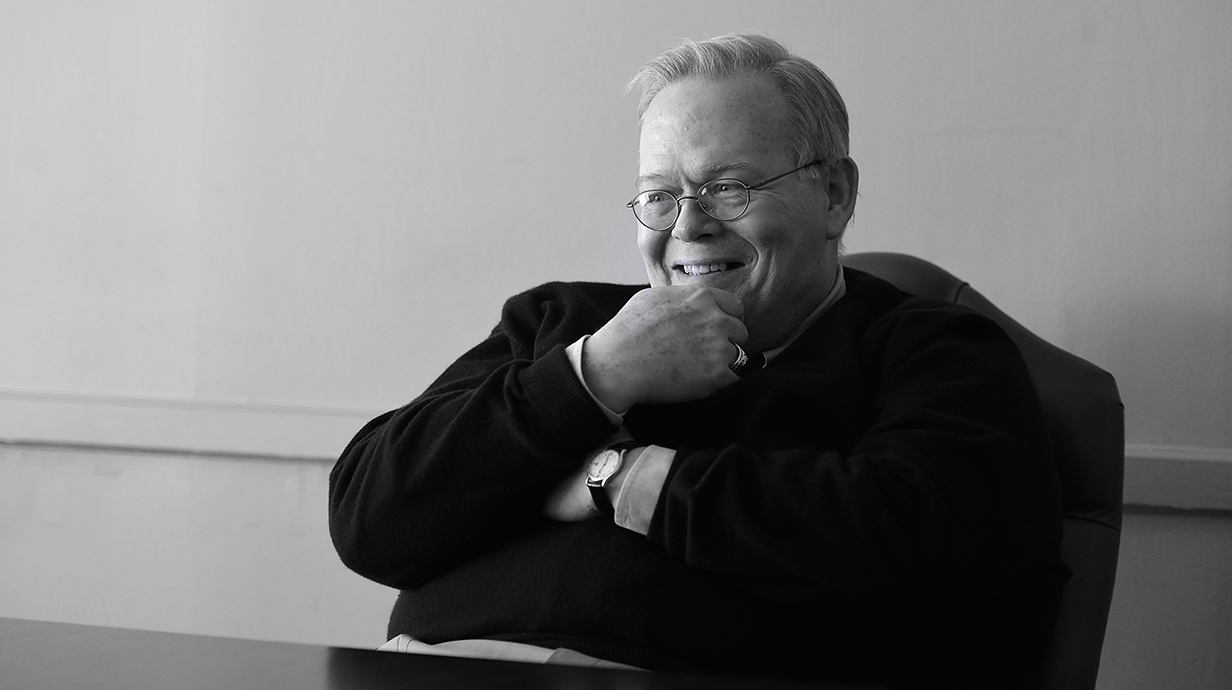 Black-and-white portrait of a man with a pensive expression sitting at a table.
