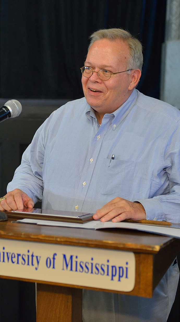 A man stands behind a lectern that has a 'University of Mississippi' sign on front.