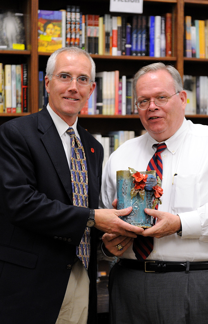 A man presents another man with a piece of pottery at an event in a bookstore.