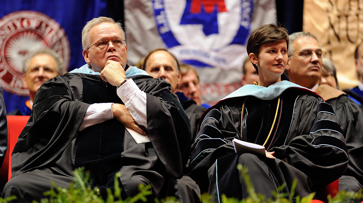 A group of people wearing academic regalia sit on a stage.