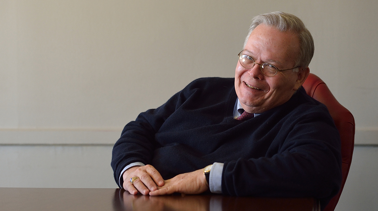 A man smiles slyly while seated at a table.