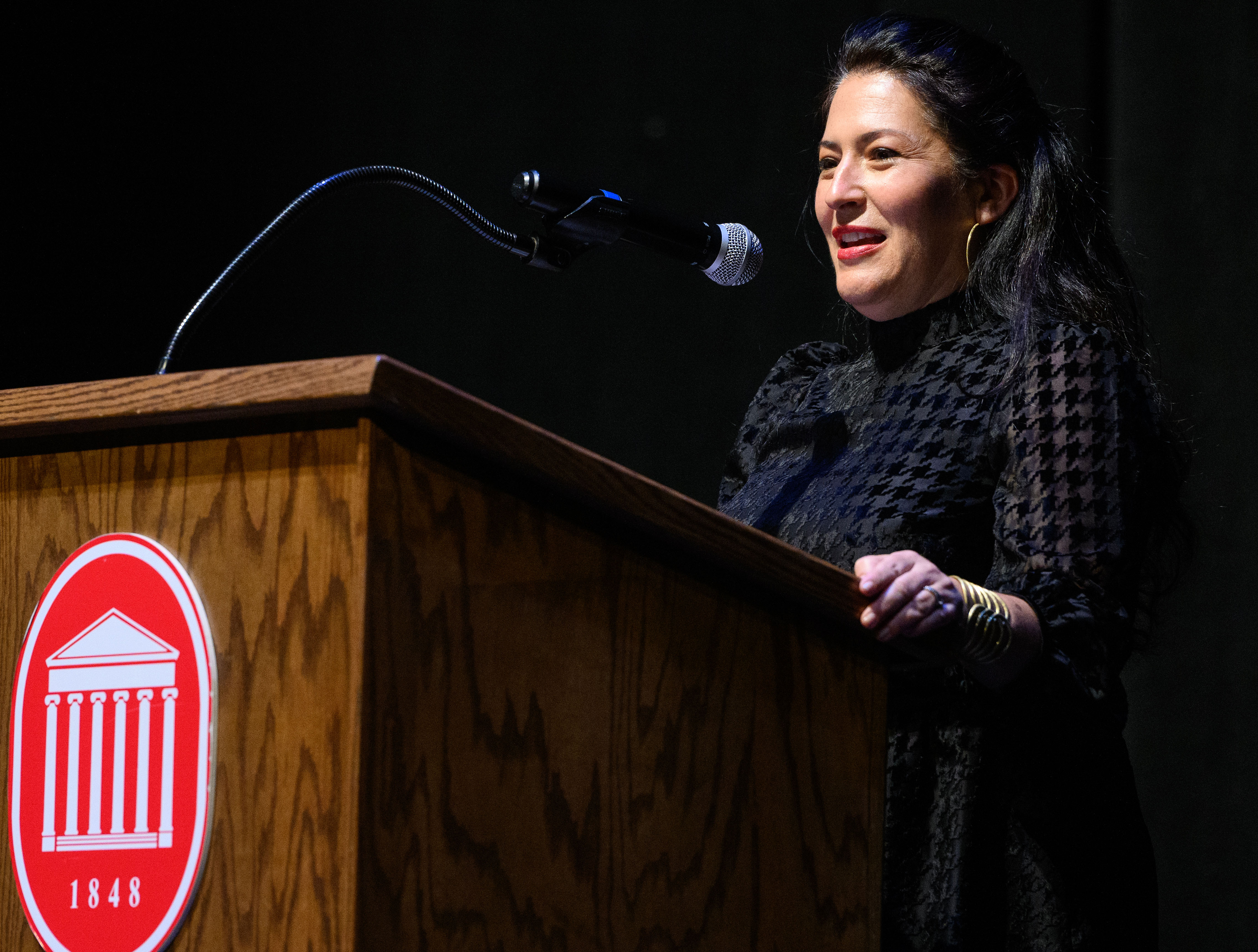 US Poet Laureate Ada Limon Speaks at a podium on a darkened stage.