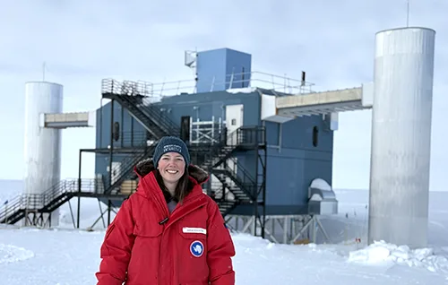 person standing in bright red coat and hat in front of observatory. Snowy conditions