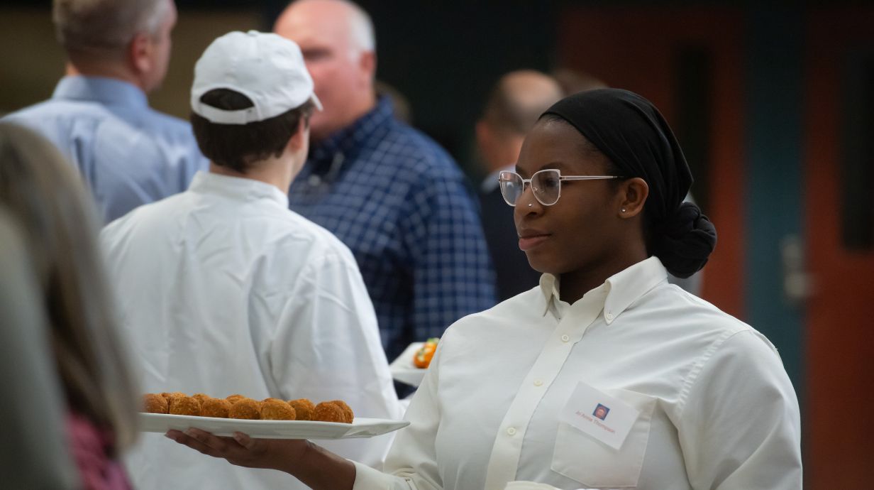 Master of Science in Hospitality Management student works in the kitchen and serving food at an event on campus. 