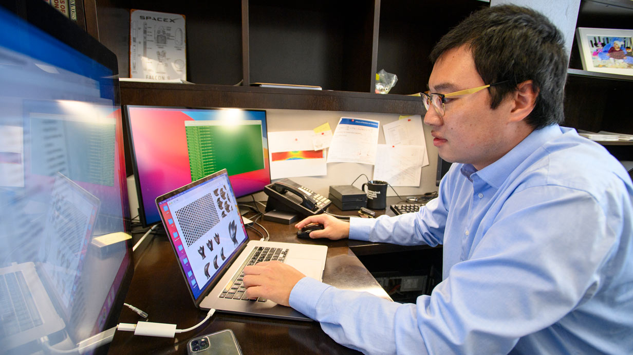 Student at a desk with a laptop and other large computer screens in front of him.