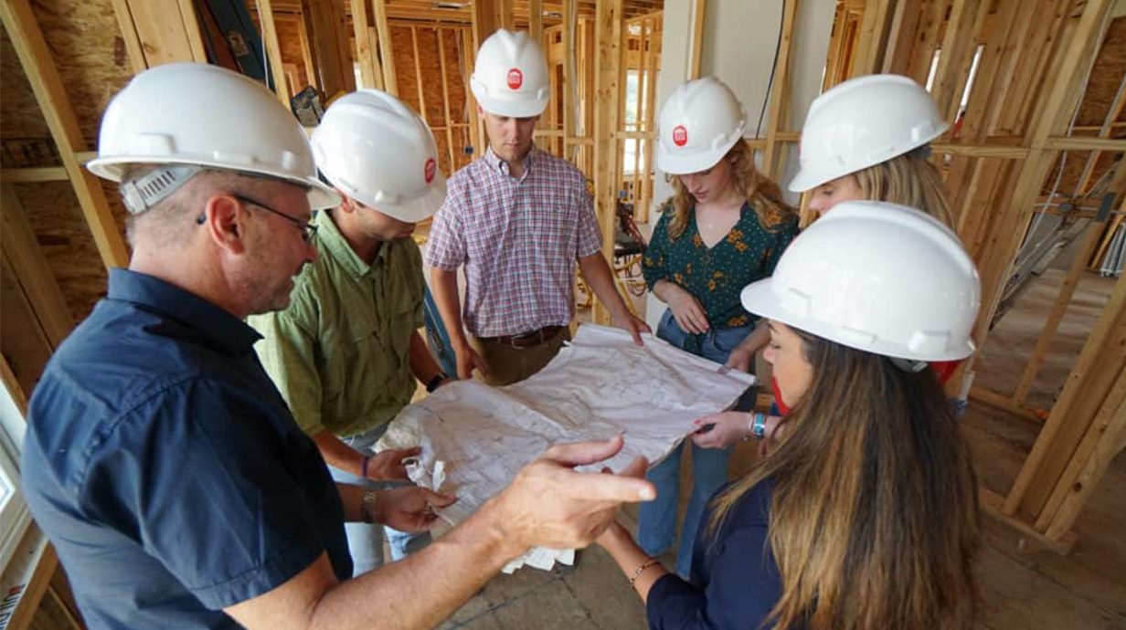  Students and a teacher looking at building plans on a construction site. 