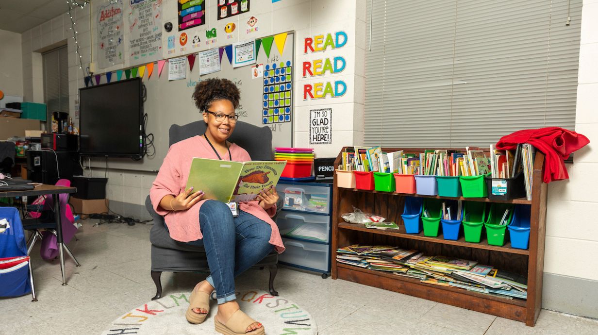 Master of Education (M.Ed.) in Elementary Education - teacher poses with book in elementary classroom.