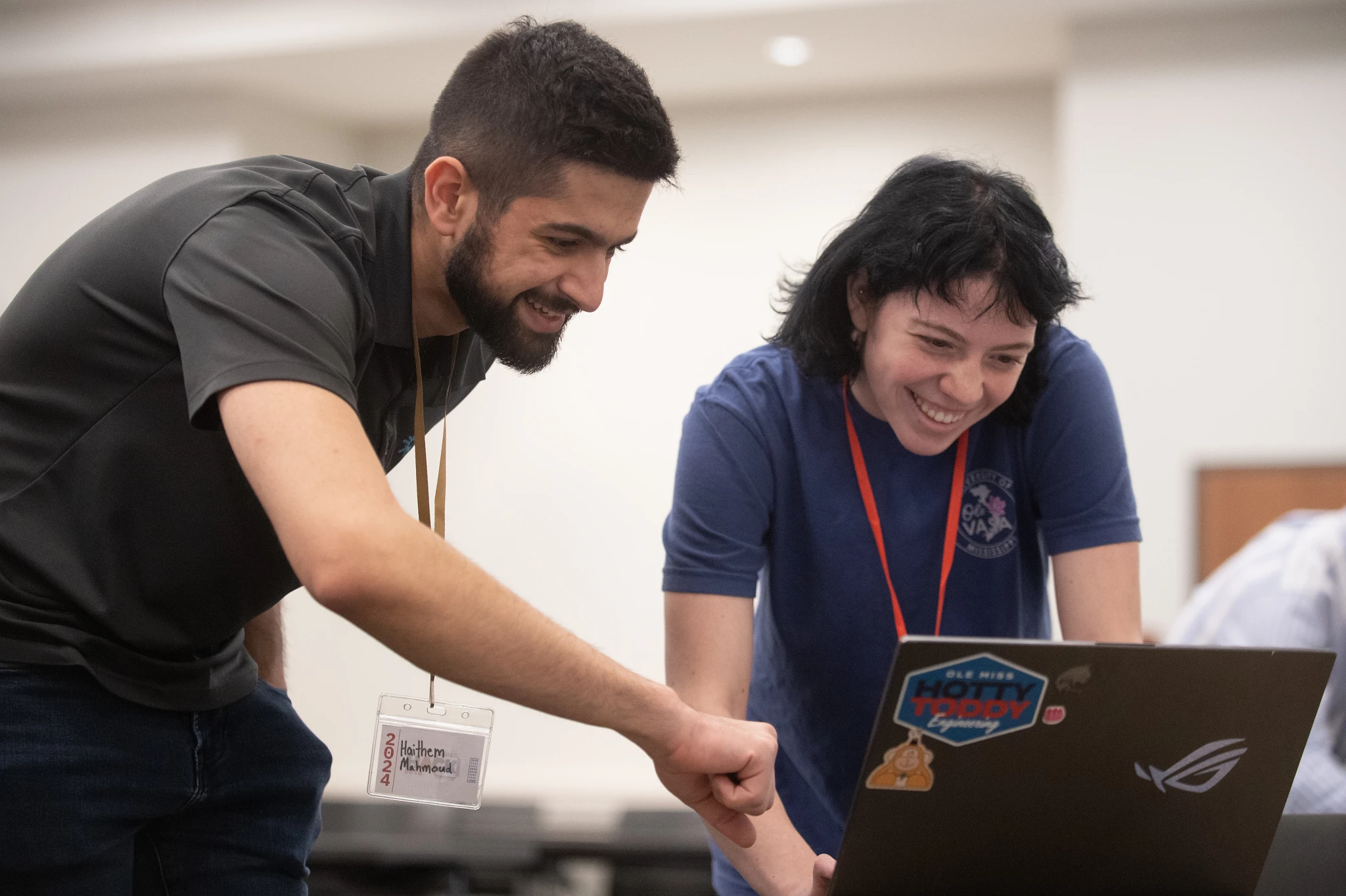 Two students smile and look intently at the screen of a laptop computer during a hack-a-thon competition.