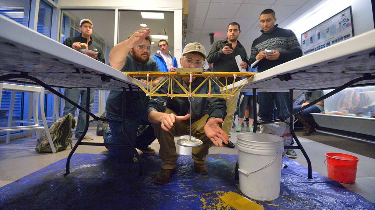 Ole Miss civil engineering students hang weights to test the strength of their bridge made from dry spaghetti noodles.