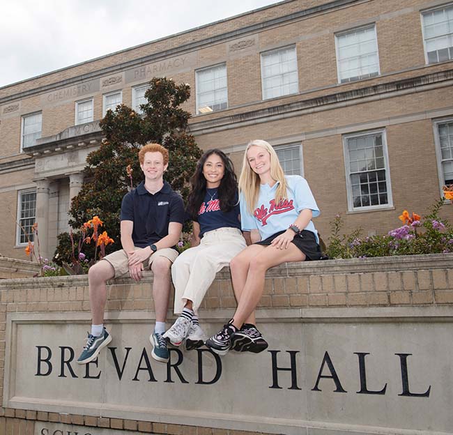 Three Ole Miss engineering students sit atop of the building sign at Brevard Hall.