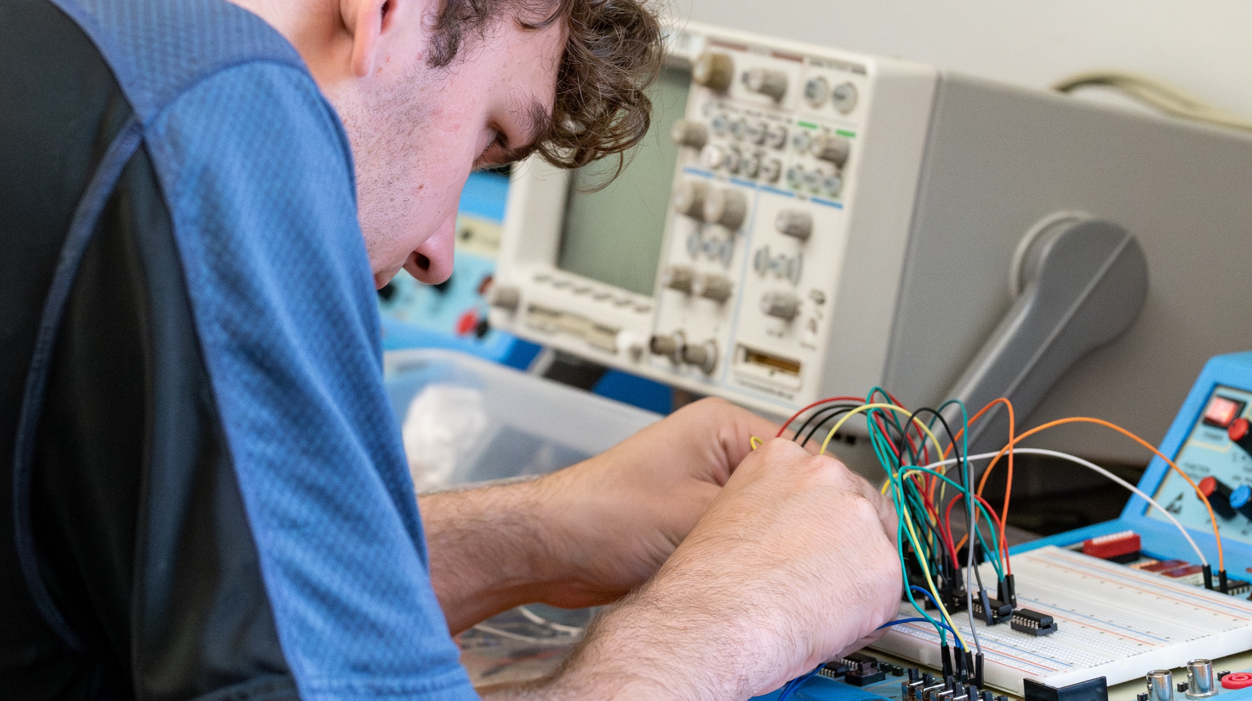 A student is closely examining a circuit board in an electrical engineering class