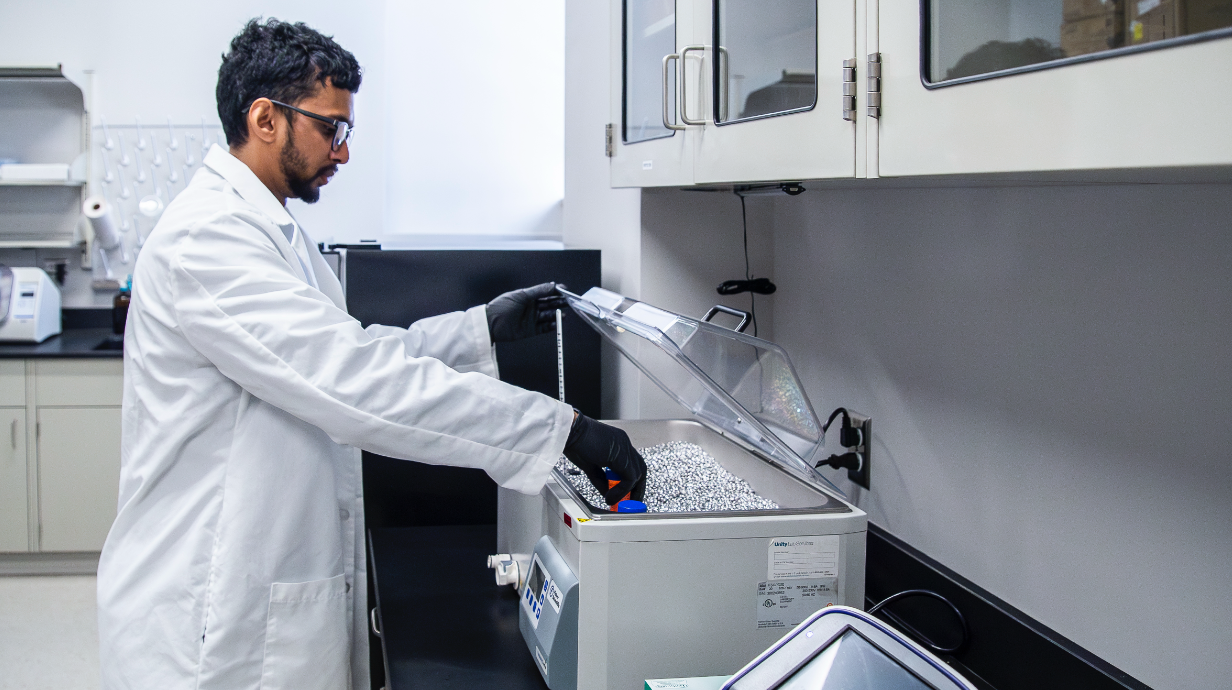 A researcher in a lab coat places items inside a container in a biomedical lab.