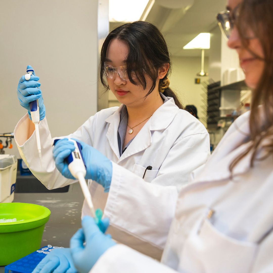 Two students in lab gear use biodevices in a biomedical lab