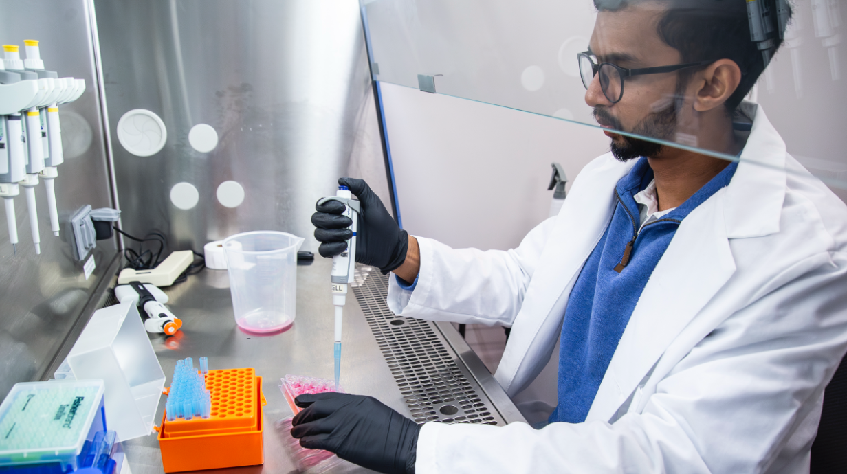 A biomedical researcher in lab gear fills samples using a handheld lab device