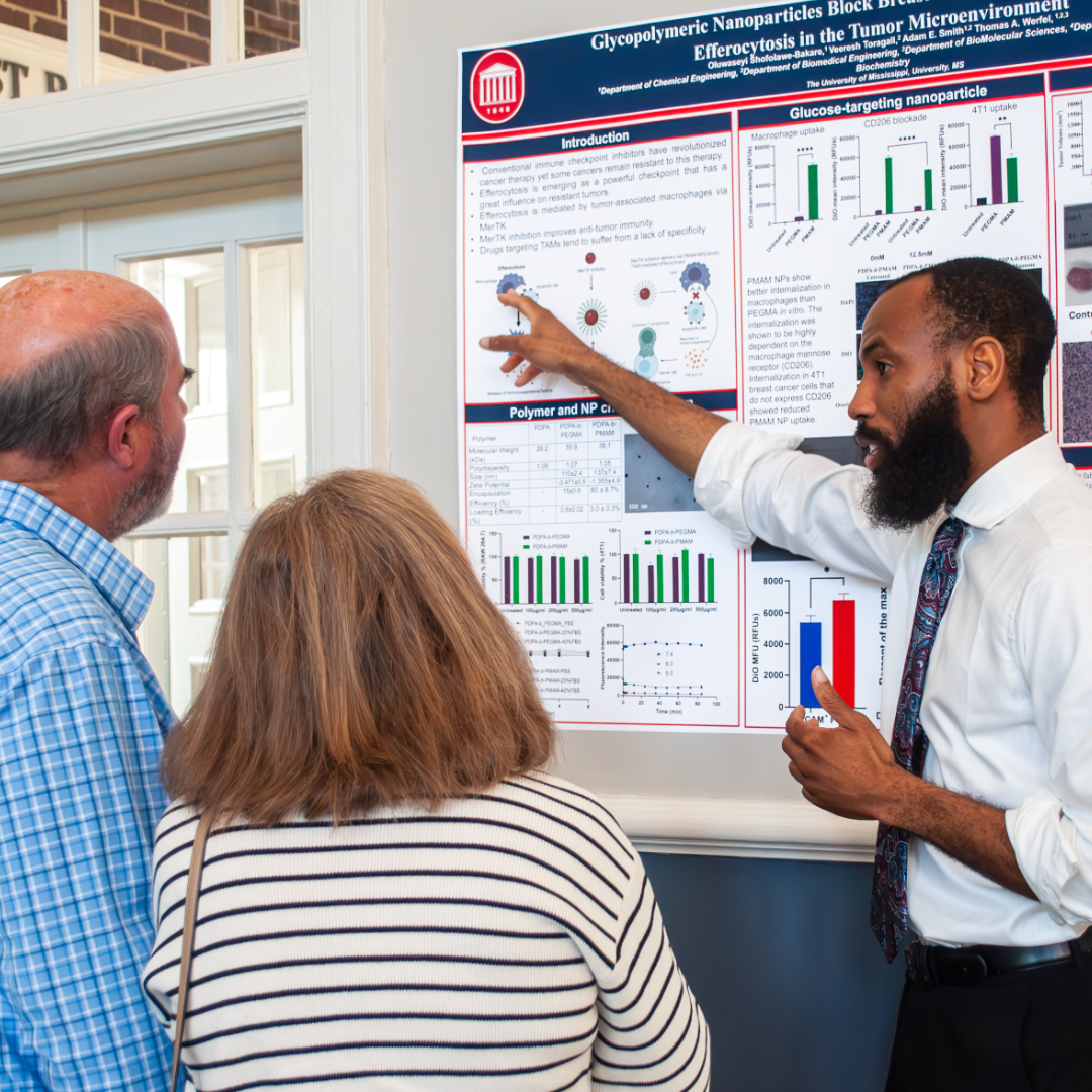 A researcher stands in front of a poster presenting a topic to 2 community members standing nearby