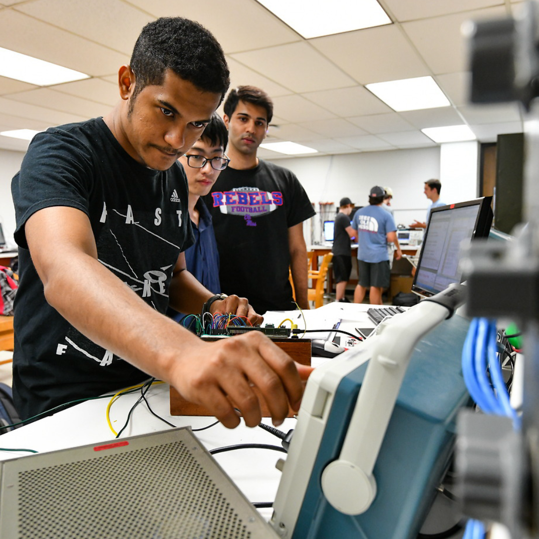 A student adjusts equipment in a classroom as other students examine from behind 