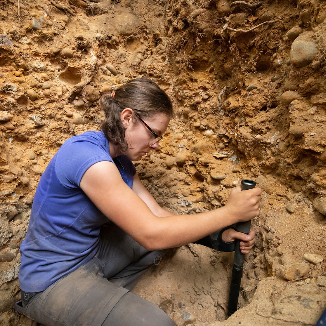 A geology student uses an instrument to dig in the dirt