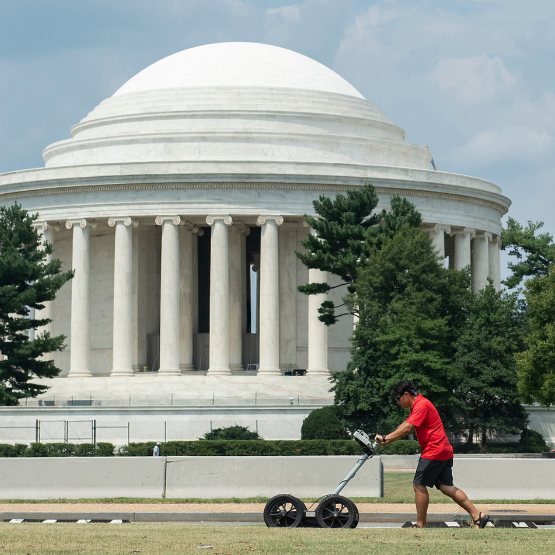 An Ole Miss student pushes an instrument to complete a land survey in Washington DC.  Historic monuments can be seen in the background.