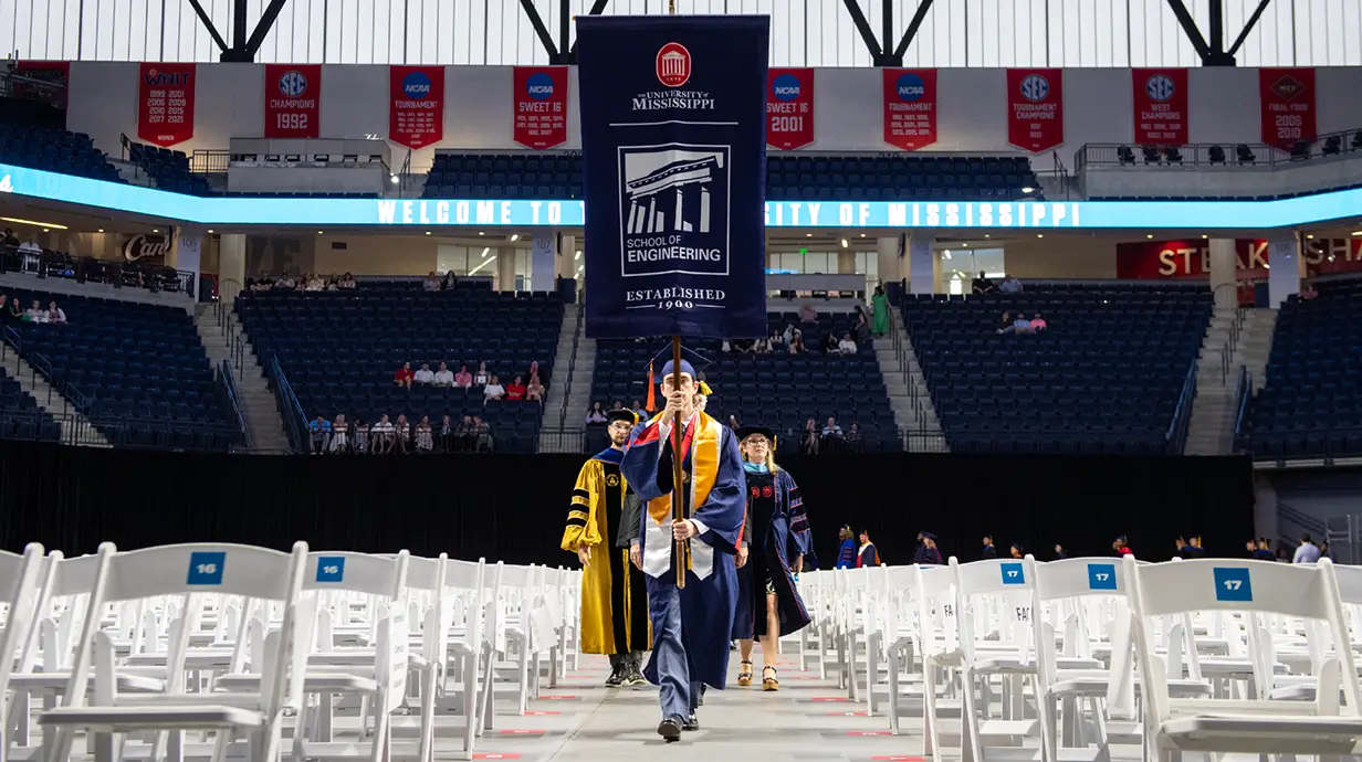 Students carry the banner of The School of Engineering during a graduation procession.