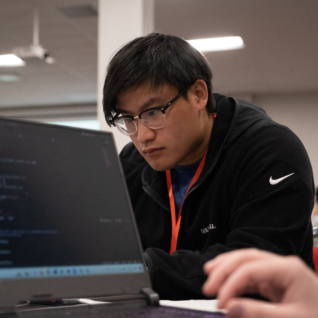 A student studies the screen of his laptop intently during a hackathon