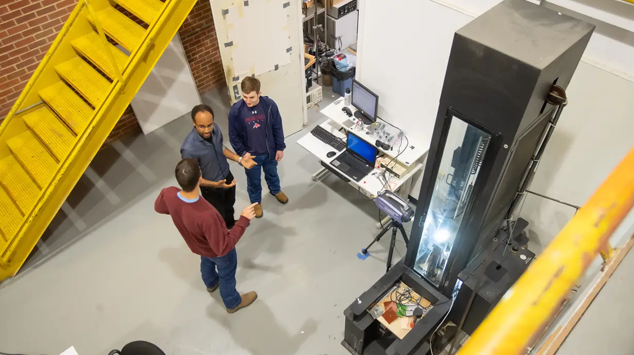 Two students talk with a professor during an engineering lab.