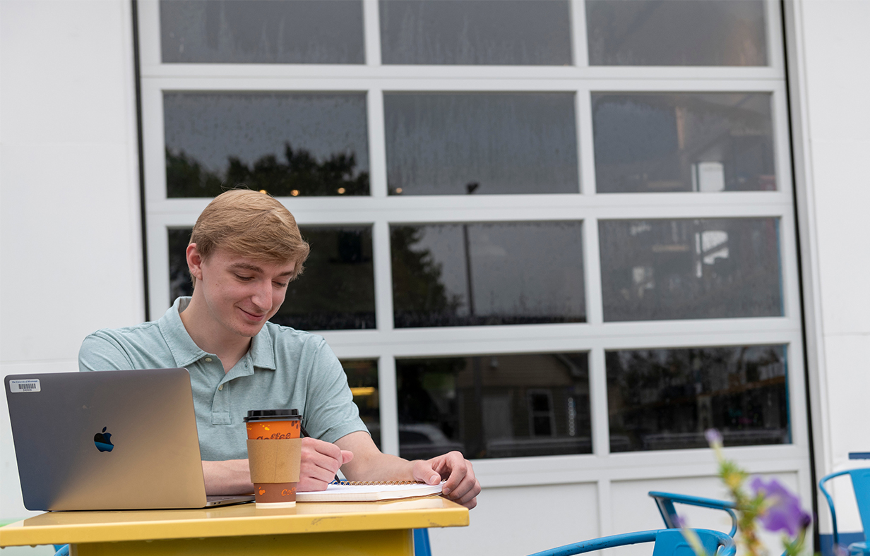Student sitting outside of a cafe with his laptop.