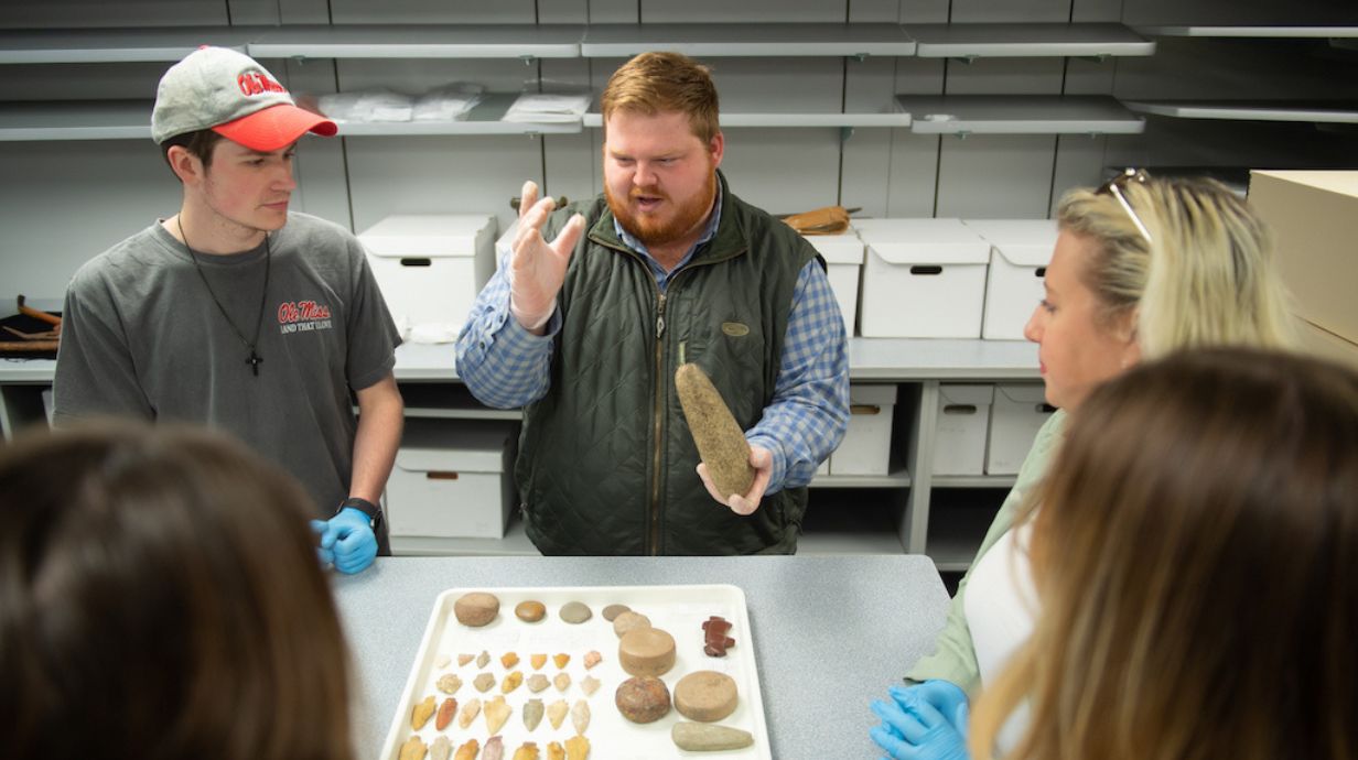 Professor discusses an array of stone tools to students. 