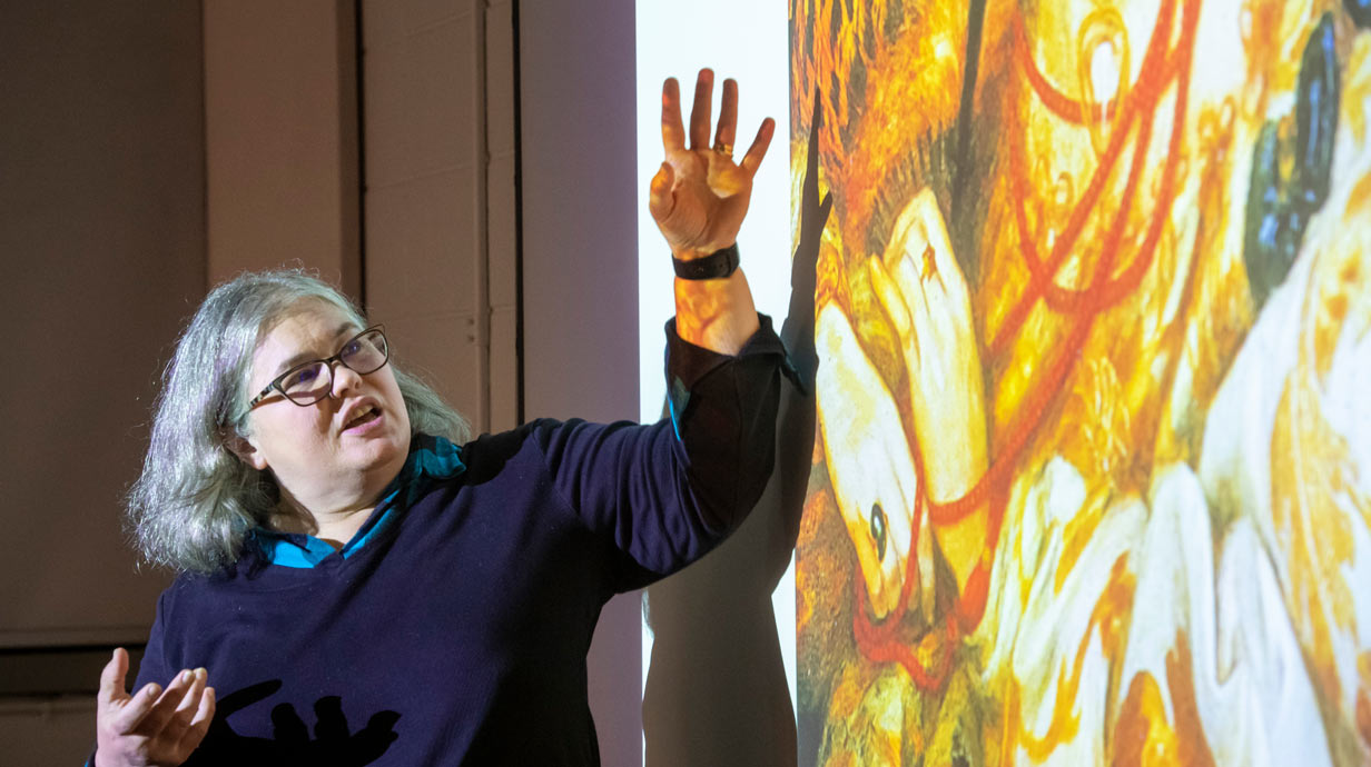 Professor Kris Belden-Adams standing in front of projected art image gesticulating with her hands.