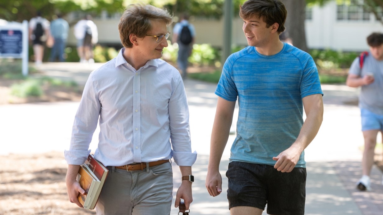 Economics faculty member and student walking and talking together outside on campus