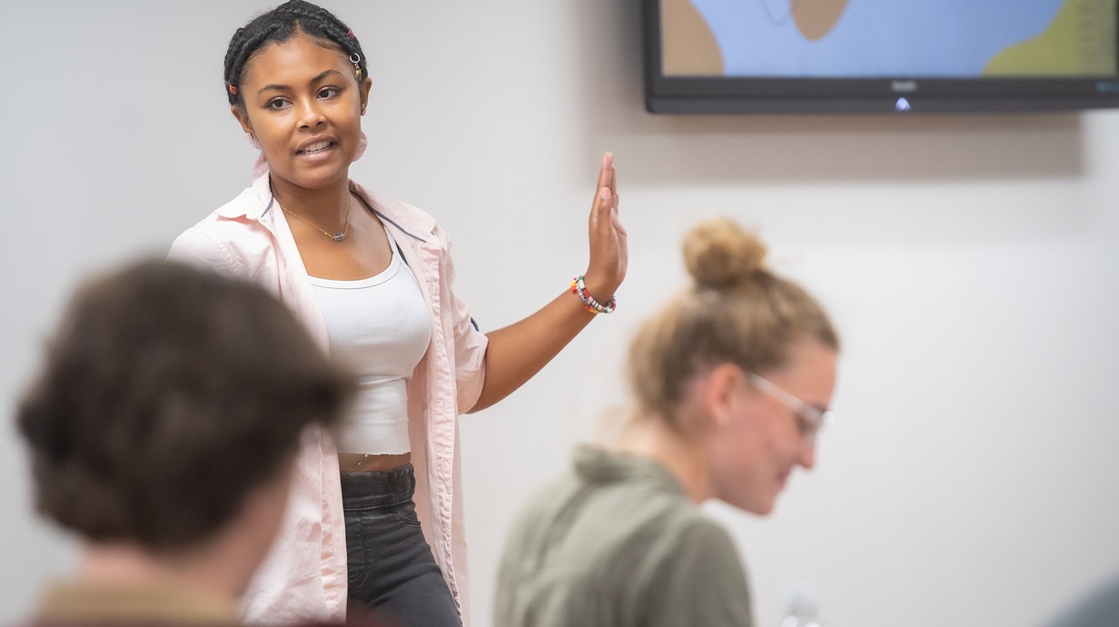 Student standing in front of class gesturing with hand.