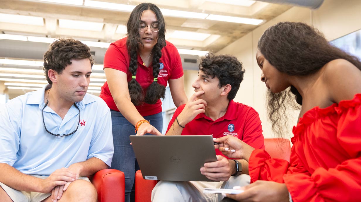 Four students around a computer having conversation
