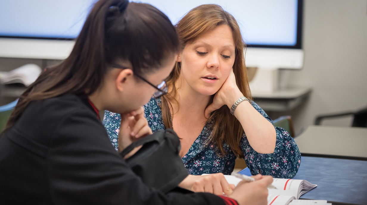 Teacher and student at table looking at book.