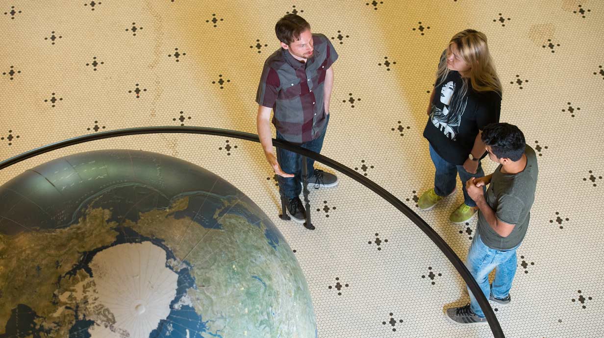 Overhead view of professor and two students next to a giant globe.