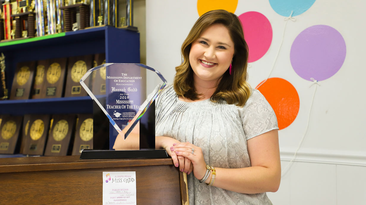 Portrait of Hannah Gadd posing with an award she's won. Award is a glass diamond shape with this writing: "The Mississippi Department of Education Recognizes Hannah Gadd as the 2019 Mississippi Teacher of the Year".