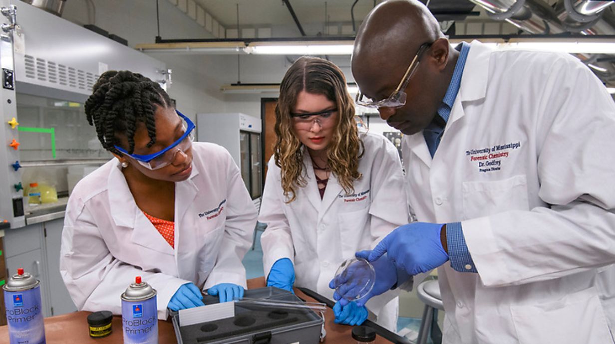 two female students work in a lab with a professor