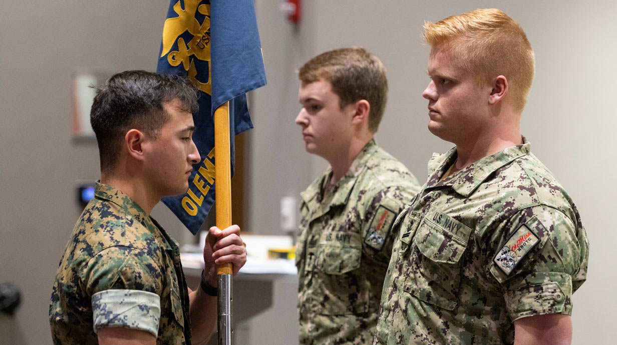 Three men in camouflage fatigues; one is holding a flag