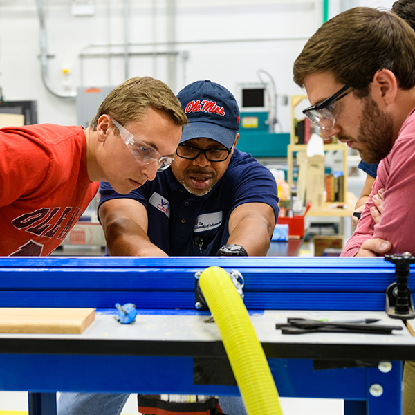An instructor demonstrates how to use a tool in a hands-on lab to two students.