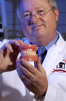 Michael A. Repka displays a transmucosal patch, placed just above the gumline (top, center) of a set of false teeth.