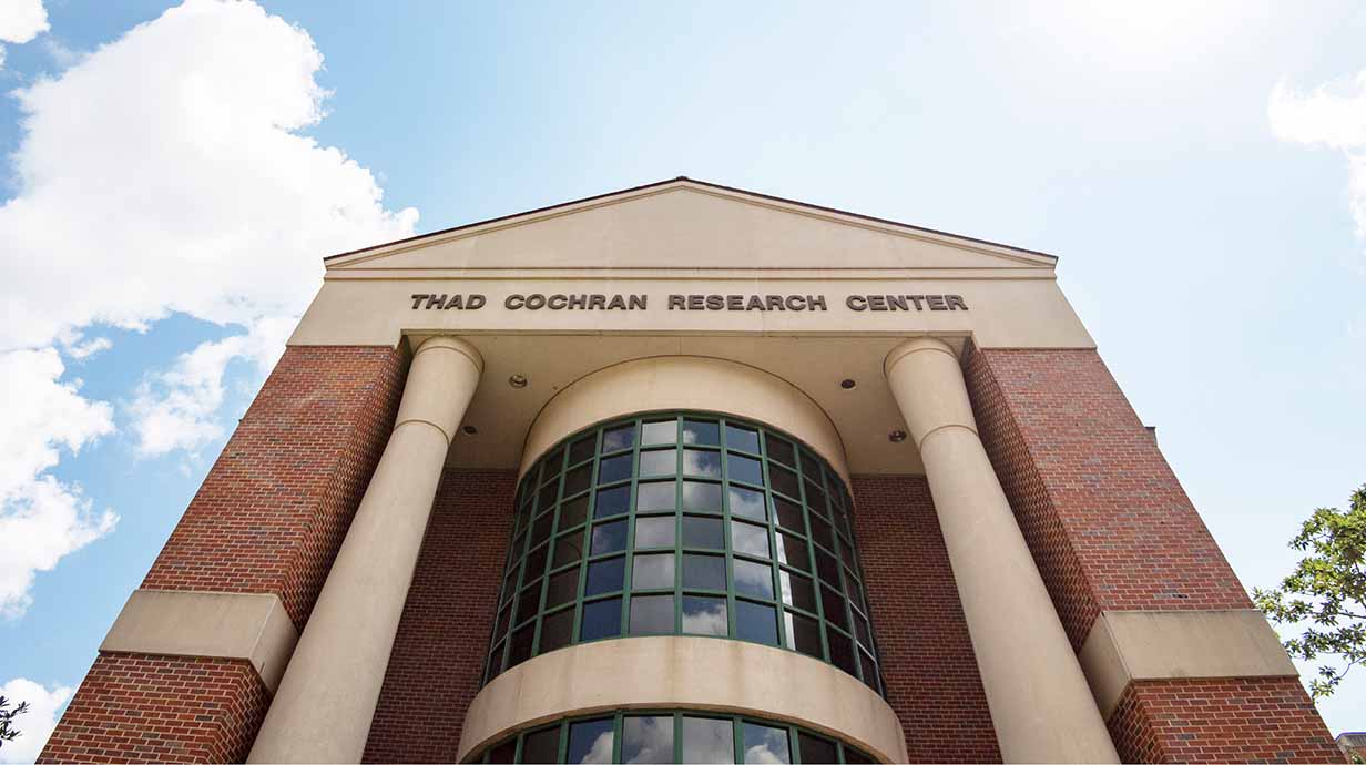 The front of the Thad Cochran Research Center is shown during mid-day with the sun overhead.