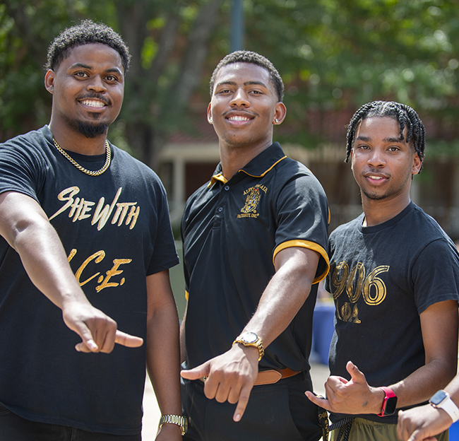 Three members of Alpha Phi Alpha use their hands for the ‘hang loose sign’, their recognized fraternal hand sign