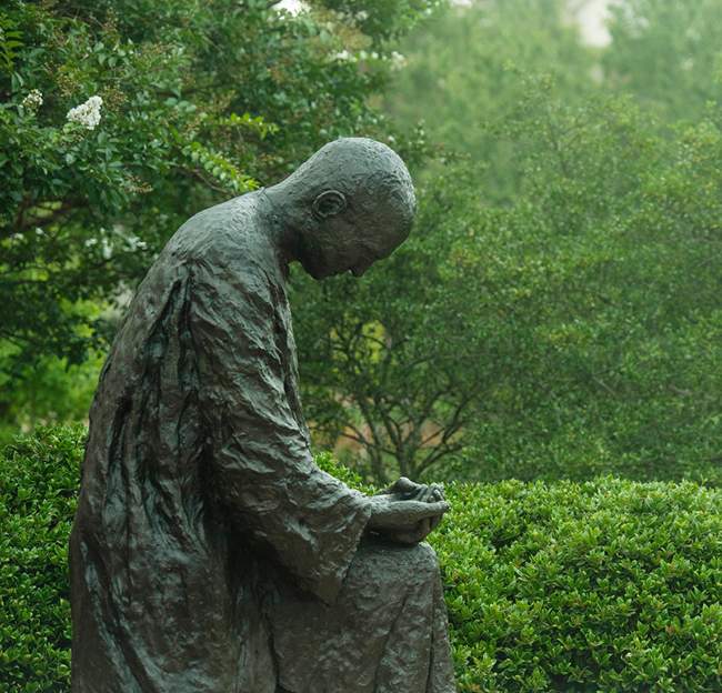 The figure kneeling in prayer of the Paris-Yates monk statue is shown on a summer morning.