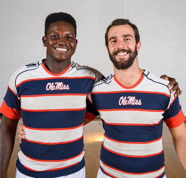 Two members of the Rugby Club pose for a photograph showcasing their new red and blue uniforms.