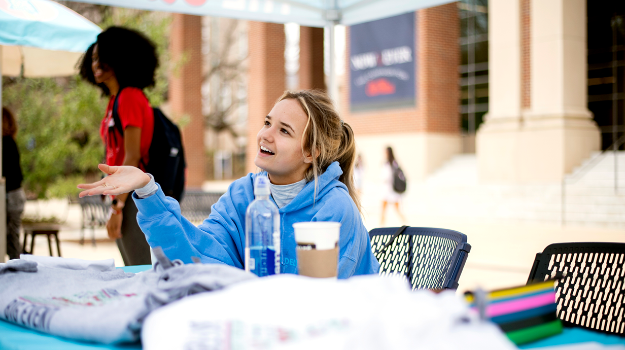 An Ole Miss Student answers questions from other students at a table set up in the Student Union Plaza.