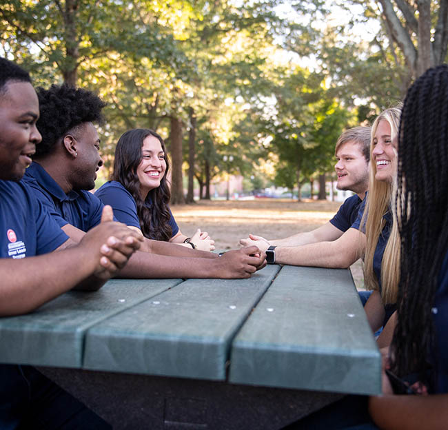 A group of Ole Miss students sit and talk at a picnic table in the Grove.