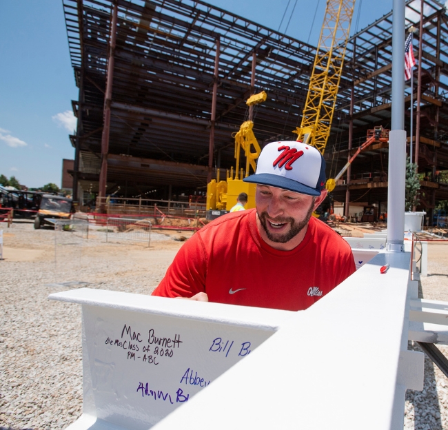 An Ole Miss alumnus signs a beam in front of the under-construction Jim and Thomas Duff Center for Science and Technology Innovation.